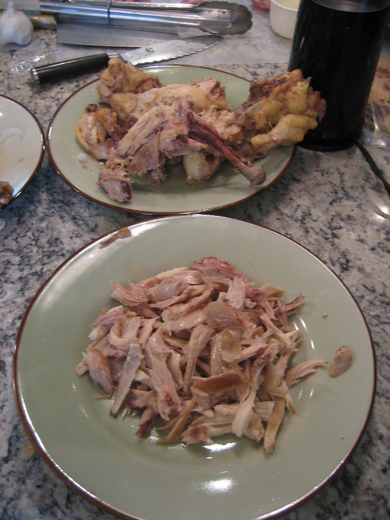Frango cozido sendo desfiado no prato para o recheio