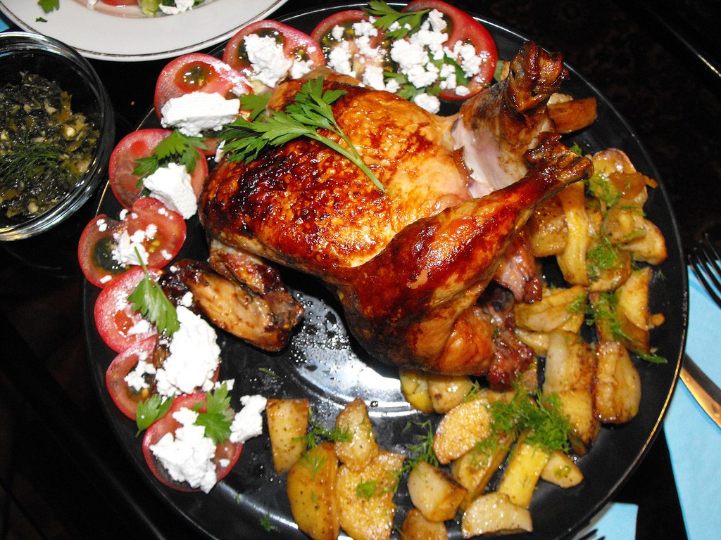 Frango assado dourado servido com batatas e tomates