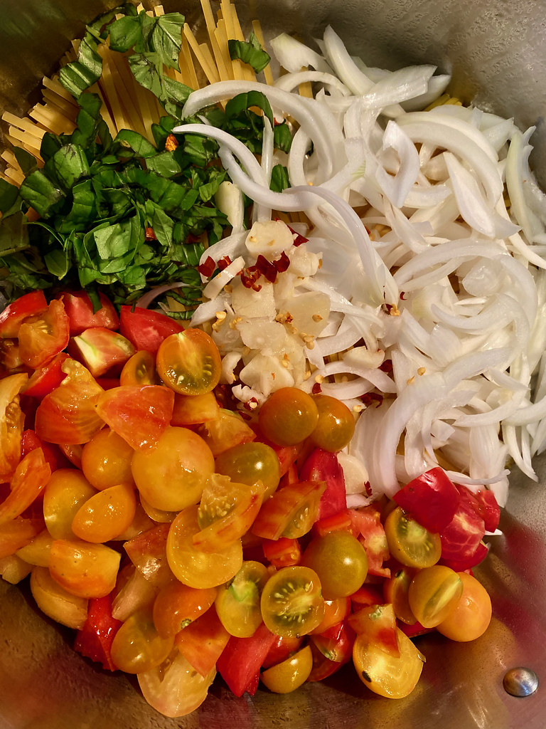 Panela com ingredientes do macarrão e tomates-cereja cortados