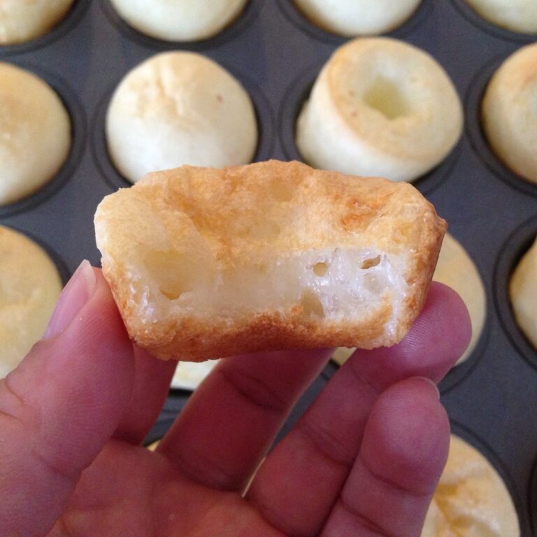 Pilha de pães de queijo dourados com café e morangos ao fundo